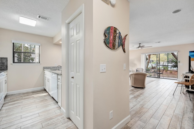 kitchen featuring white cabinets, white dishwasher, light hardwood / wood-style flooring, ceiling fan, and a textured ceiling