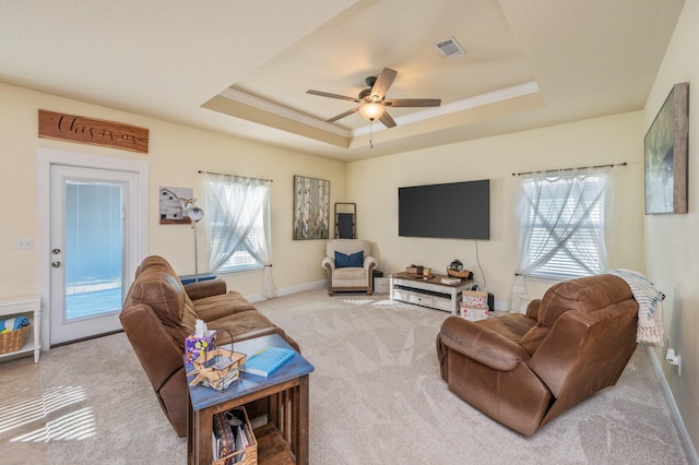 living room with a raised ceiling, ceiling fan, plenty of natural light, and light colored carpet