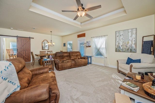 carpeted living room with ceiling fan with notable chandelier, a barn door, a raised ceiling, and crown molding