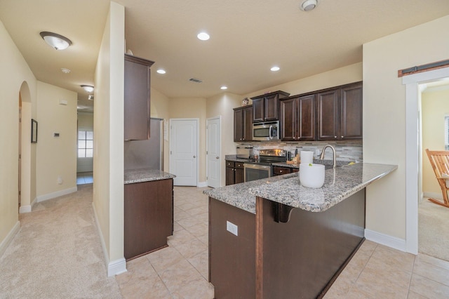 kitchen featuring a kitchen breakfast bar, light stone countertops, dark brown cabinets, kitchen peninsula, and stainless steel appliances