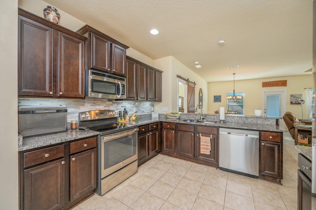 kitchen with a barn door, kitchen peninsula, decorative light fixtures, and appliances with stainless steel finishes