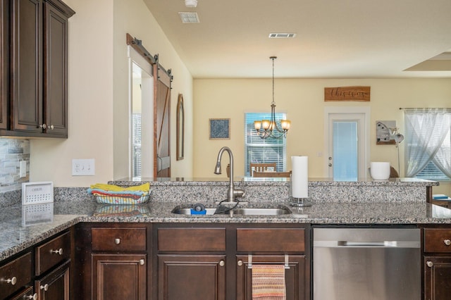 kitchen featuring stainless steel dishwasher, dark stone counters, sink, a barn door, and a chandelier