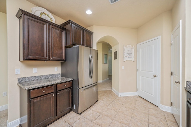 kitchen with stainless steel fridge, dark brown cabinets, and light tile patterned floors