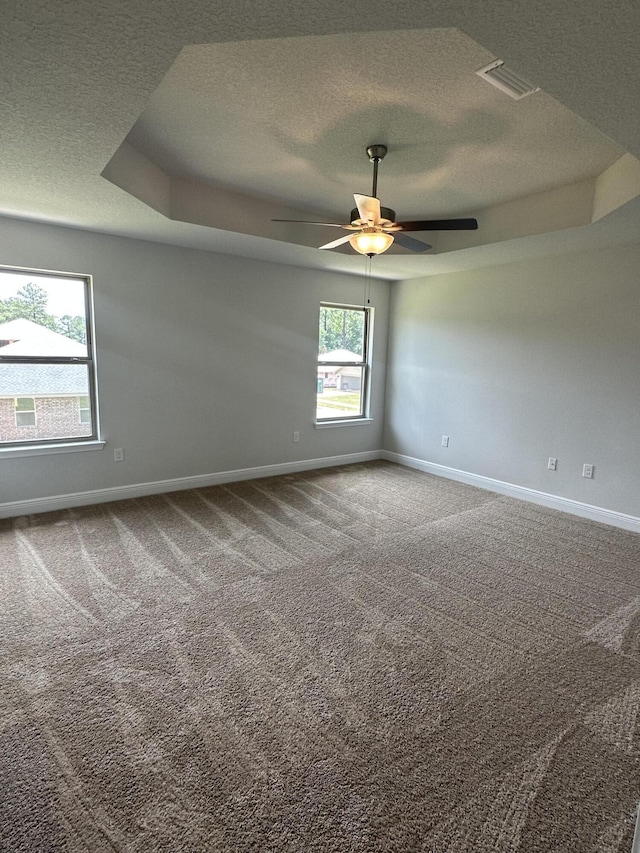 carpeted empty room featuring a raised ceiling, ceiling fan, and a textured ceiling