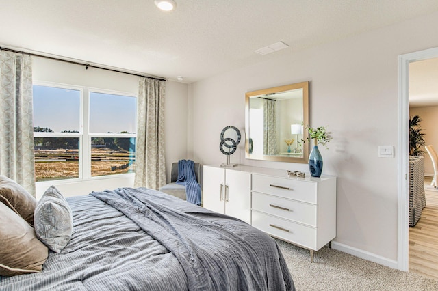 bedroom featuring light colored carpet, a textured ceiling, and baseboards