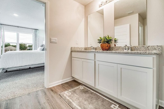 full bath featuring double vanity, a sink, ensuite bath, wood finished floors, and baseboards