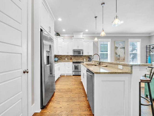 kitchen with white cabinets, sink, appliances with stainless steel finishes, light hardwood / wood-style floors, and a breakfast bar area