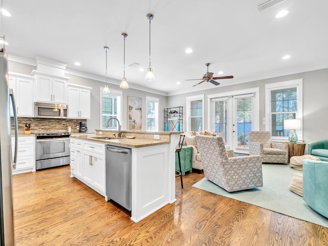 kitchen featuring appliances with stainless steel finishes, light wood-type flooring, a kitchen island with sink, decorative light fixtures, and white cabinetry