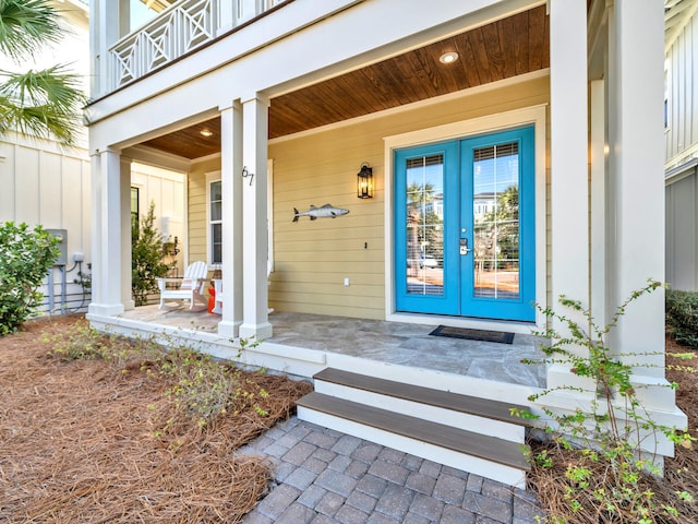 view of exterior entry with a porch, a balcony, and french doors