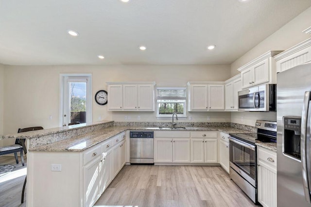 kitchen featuring white cabinetry, kitchen peninsula, a kitchen bar, appliances with stainless steel finishes, and light wood-type flooring