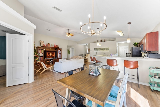 dining space with ceiling fan with notable chandelier, light hardwood / wood-style floors, and vaulted ceiling