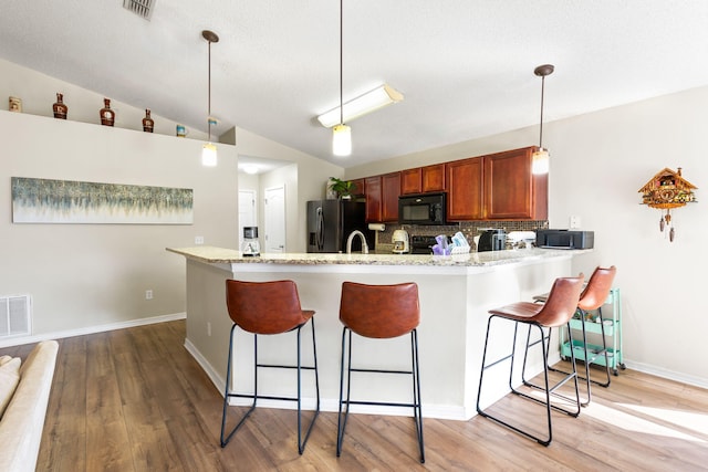 kitchen featuring kitchen peninsula, vaulted ceiling, black appliances, decorative light fixtures, and light hardwood / wood-style flooring