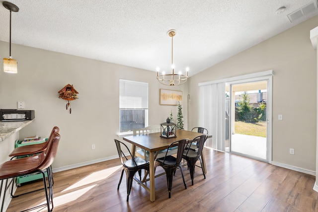 dining space featuring a textured ceiling, hardwood / wood-style flooring, vaulted ceiling, and a notable chandelier