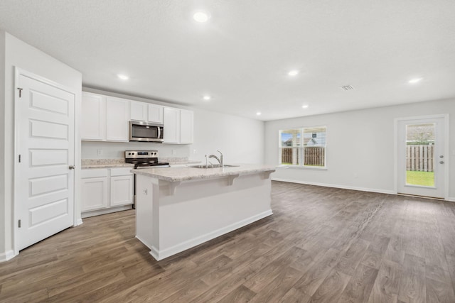 kitchen with white cabinets, appliances with stainless steel finishes, dark hardwood / wood-style floors, and an island with sink