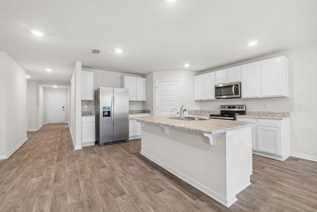 kitchen with appliances with stainless steel finishes, light wood-type flooring, a kitchen island with sink, sink, and white cabinets