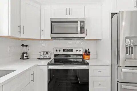 kitchen featuring decorative backsplash, white cabinetry, and appliances with stainless steel finishes