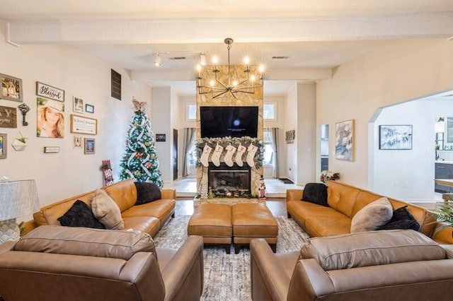 living room with beam ceiling, a stone fireplace, and a chandelier