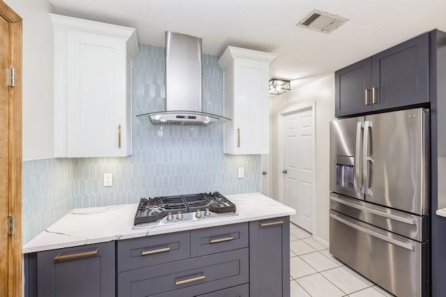 kitchen featuring white cabinetry, wall chimney exhaust hood, backsplash, light tile patterned floors, and appliances with stainless steel finishes