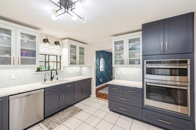 kitchen featuring appliances with stainless steel finishes, light stone counters, sink, white cabinets, and light tile patterned flooring