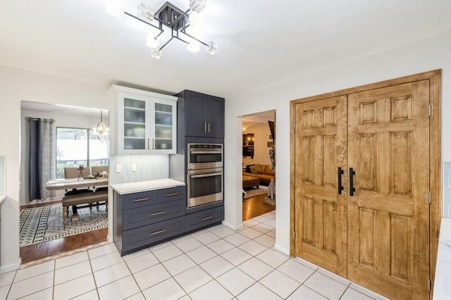 kitchen featuring light tile patterned floors, stainless steel double oven, white cabinetry, and backsplash