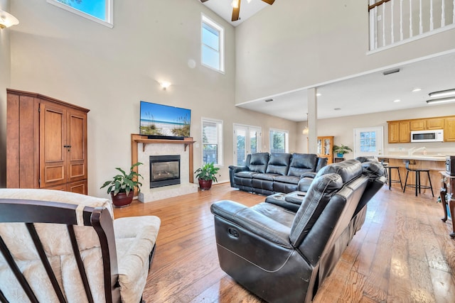 living room with a towering ceiling, ceiling fan, and light hardwood / wood-style flooring