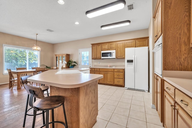 kitchen with white appliances, hanging light fixtures, an island with sink, a breakfast bar, and sink