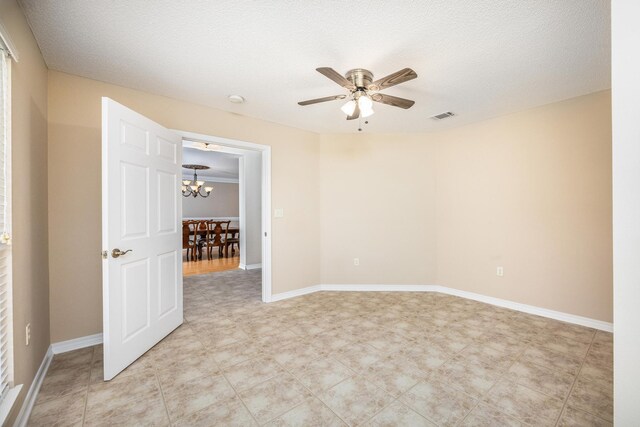 empty room featuring a textured ceiling and ceiling fan with notable chandelier