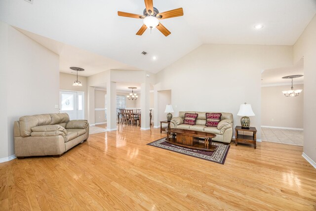 living room with ceiling fan with notable chandelier, hardwood / wood-style flooring, and vaulted ceiling