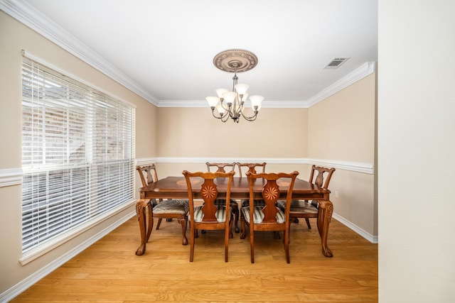 dining space with light hardwood / wood-style flooring, ornamental molding, and a notable chandelier