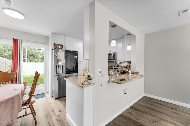 kitchen with kitchen peninsula, light wood-type flooring, stainless steel appliances, pendant lighting, and white cabinetry