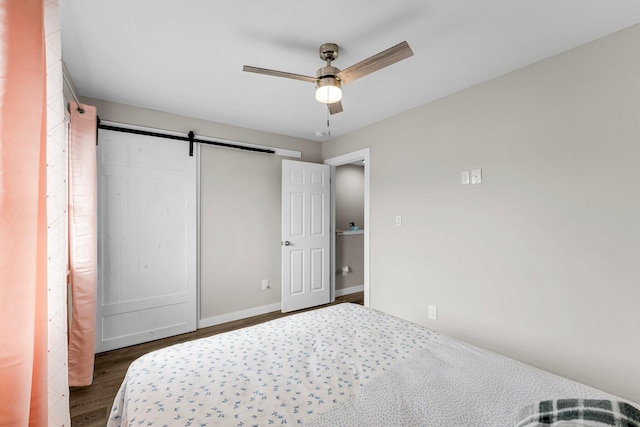 bedroom with ceiling fan, a barn door, and dark wood-type flooring