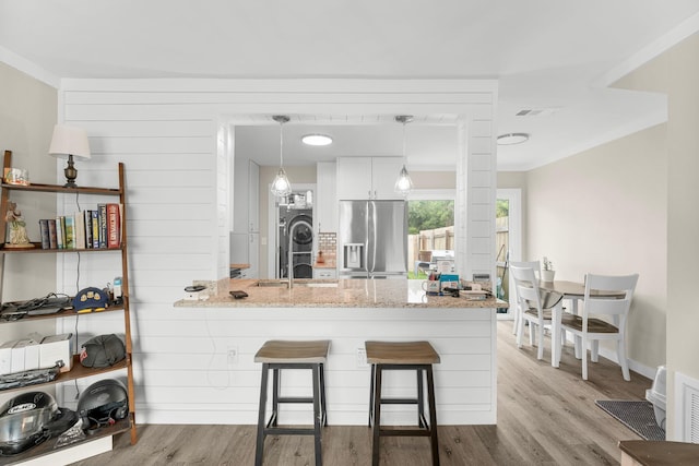 kitchen featuring stainless steel refrigerator with ice dispenser, a breakfast bar, light hardwood / wood-style flooring, stacked washer and dryer, and white cabinetry