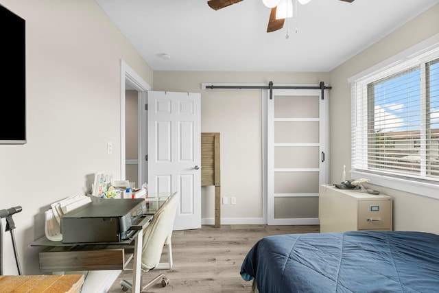 bedroom featuring ceiling fan, a barn door, and light wood-type flooring