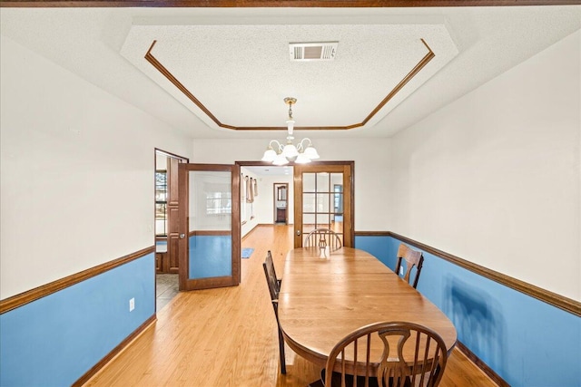 dining room with french doors, a textured ceiling, a raised ceiling, light hardwood / wood-style flooring, and a notable chandelier