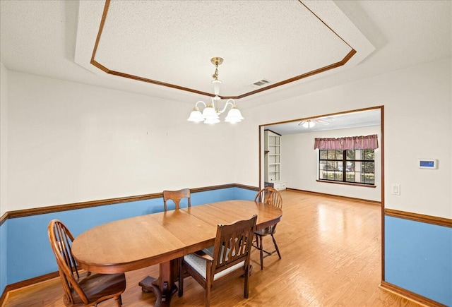 dining room with a raised ceiling, hardwood / wood-style floors, a textured ceiling, and an inviting chandelier