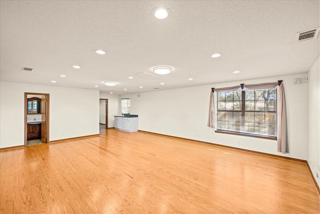 unfurnished living room with light wood-type flooring and a textured ceiling