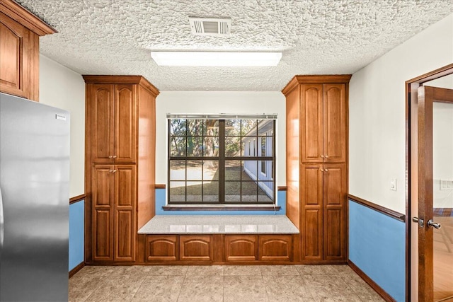 kitchen with a textured ceiling, stainless steel refrigerator, and light tile patterned flooring