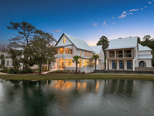 back house at dusk featuring a balcony and a water view