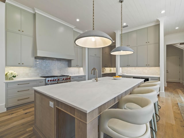 kitchen featuring sink, hardwood / wood-style floors, an island with sink, decorative backsplash, and high end stainless steel range