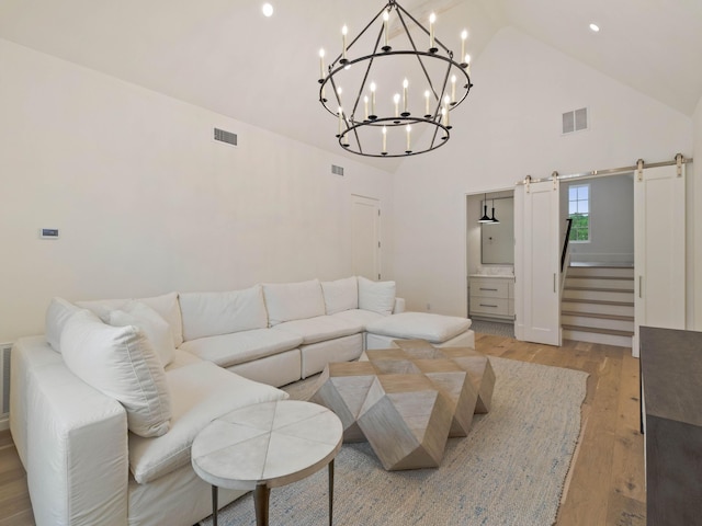 living room with a barn door, light hardwood / wood-style floors, and high vaulted ceiling