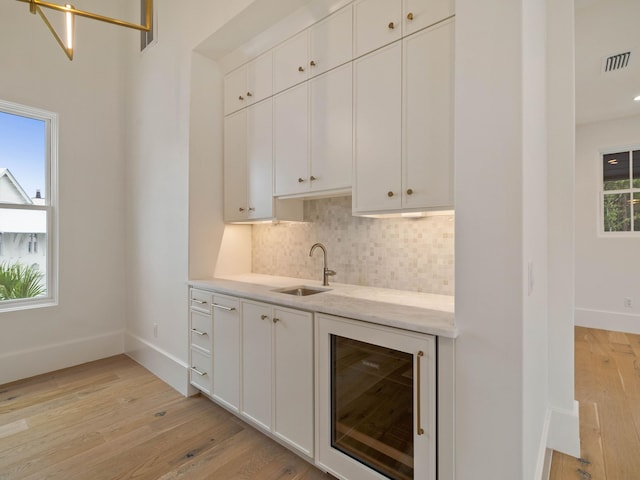 bar featuring light stone countertops, light wood-type flooring, wine cooler, sink, and white cabinetry