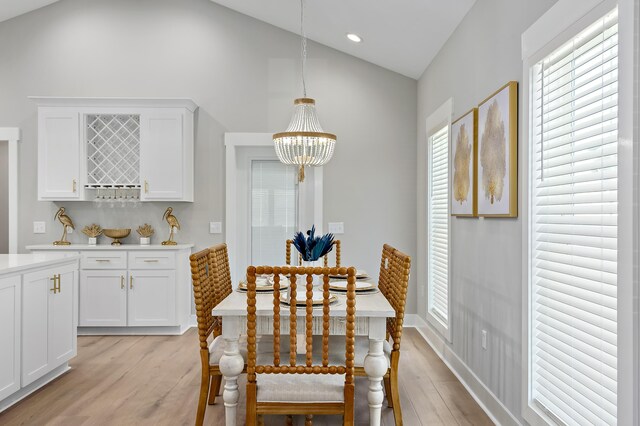 dining area with a chandelier, light wood-type flooring, and vaulted ceiling