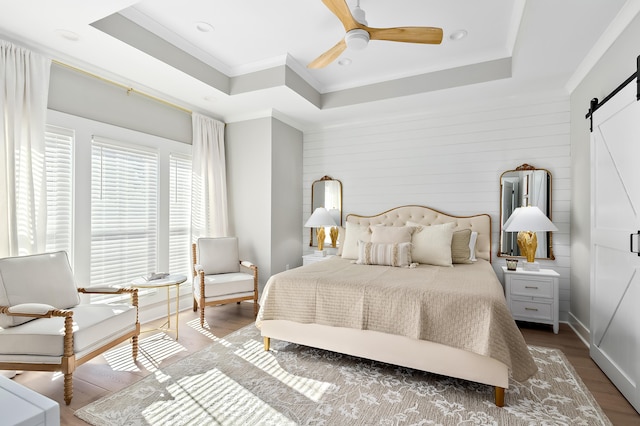 bedroom with a raised ceiling, a barn door, ceiling fan, and hardwood / wood-style flooring