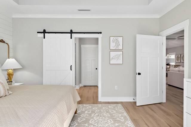 bedroom with light wood-type flooring, ensuite bath, crown molding, a barn door, and a closet