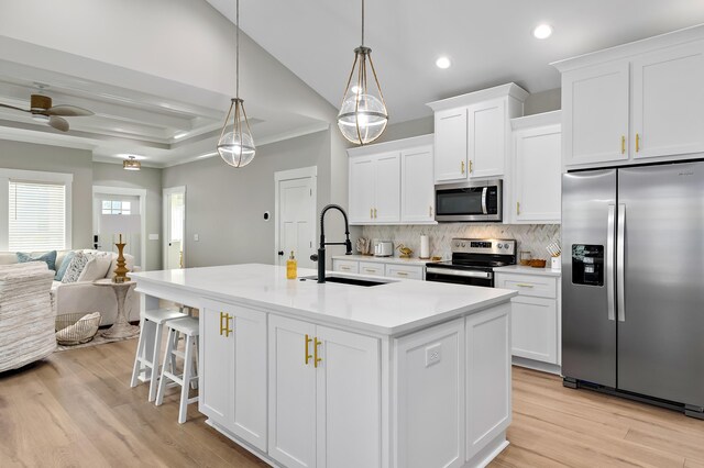 kitchen with appliances with stainless steel finishes, a center island with sink, light hardwood / wood-style floors, white cabinetry, and hanging light fixtures