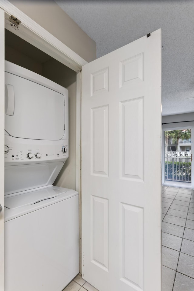 laundry room featuring stacked washing maching and dryer, a textured ceiling, and light tile patterned floors