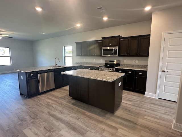 kitchen with kitchen peninsula, light wood-type flooring, stainless steel appliances, sink, and a center island