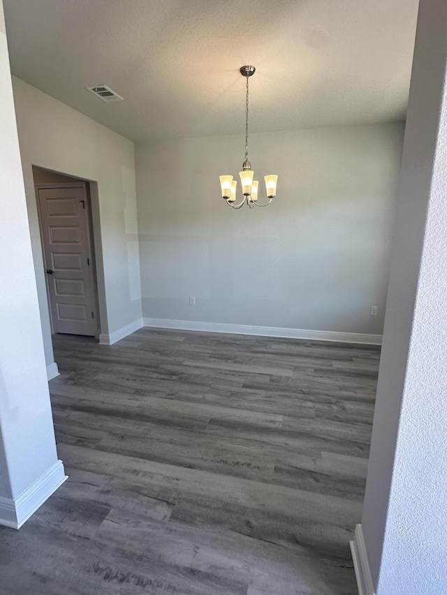 spare room featuring a textured ceiling, an inviting chandelier, and dark wood-type flooring