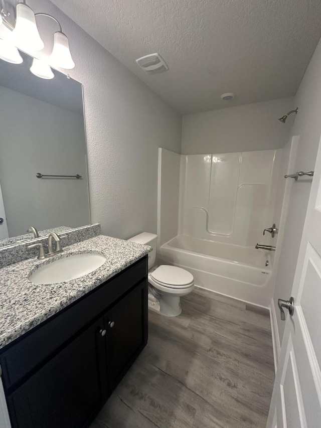 full bathroom featuring bathtub / shower combination, vanity, a textured ceiling, hardwood / wood-style flooring, and toilet