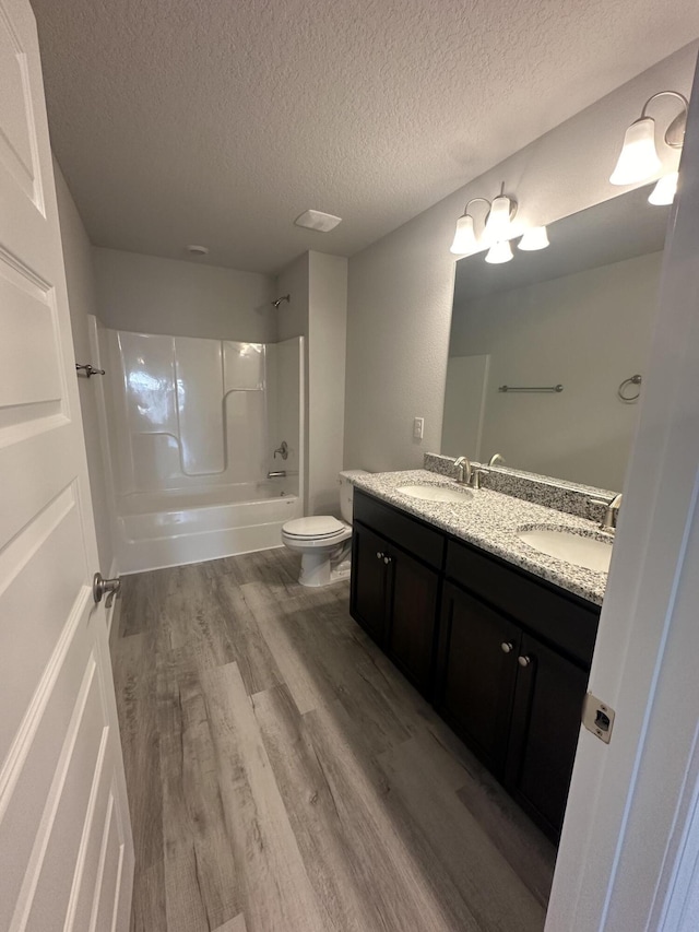 full bathroom featuring washtub / shower combination, hardwood / wood-style floors, a textured ceiling, toilet, and vanity